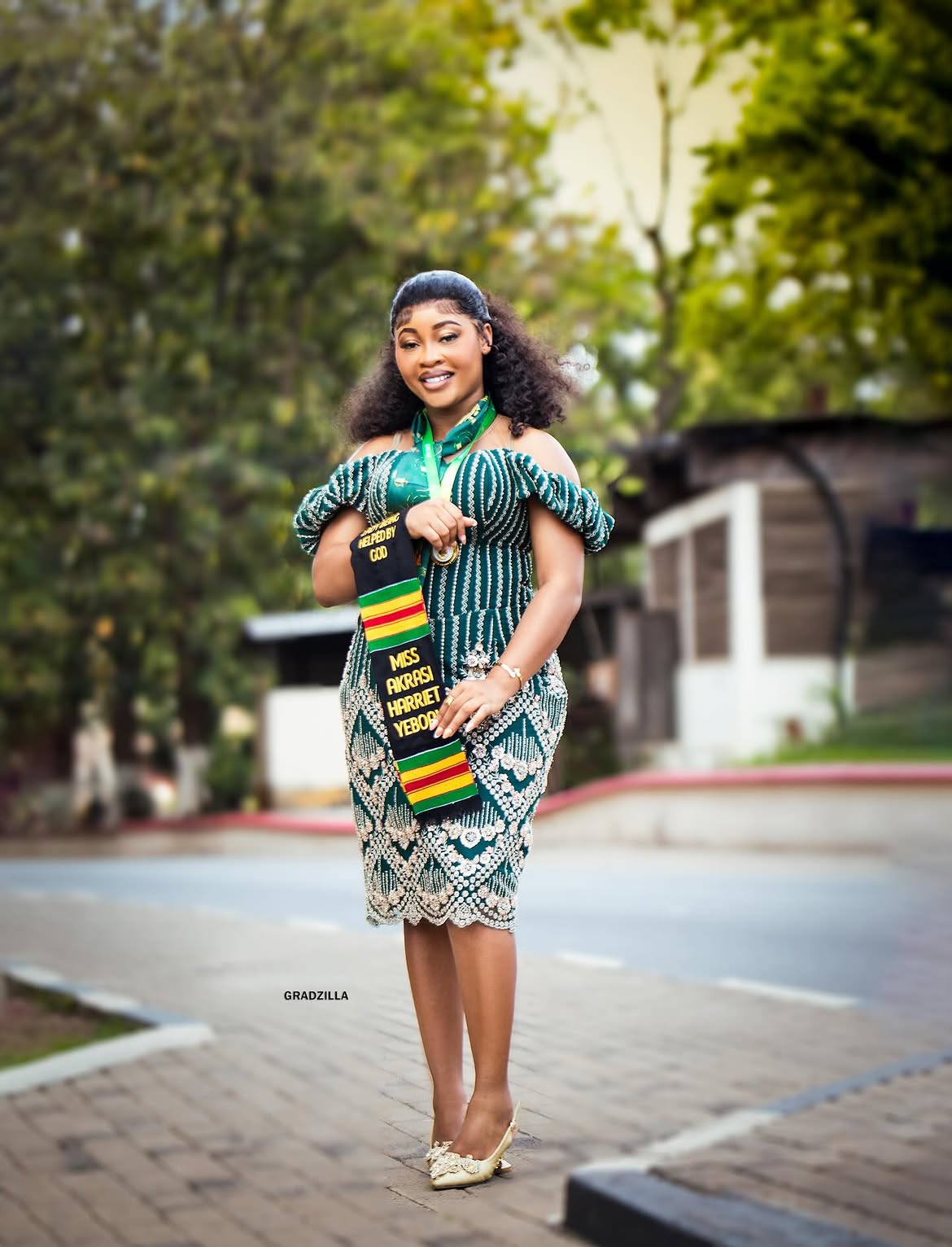 Ghanaian graduate Miss Harriet Yeboah walking confidently in a beaded green kente dress on campus