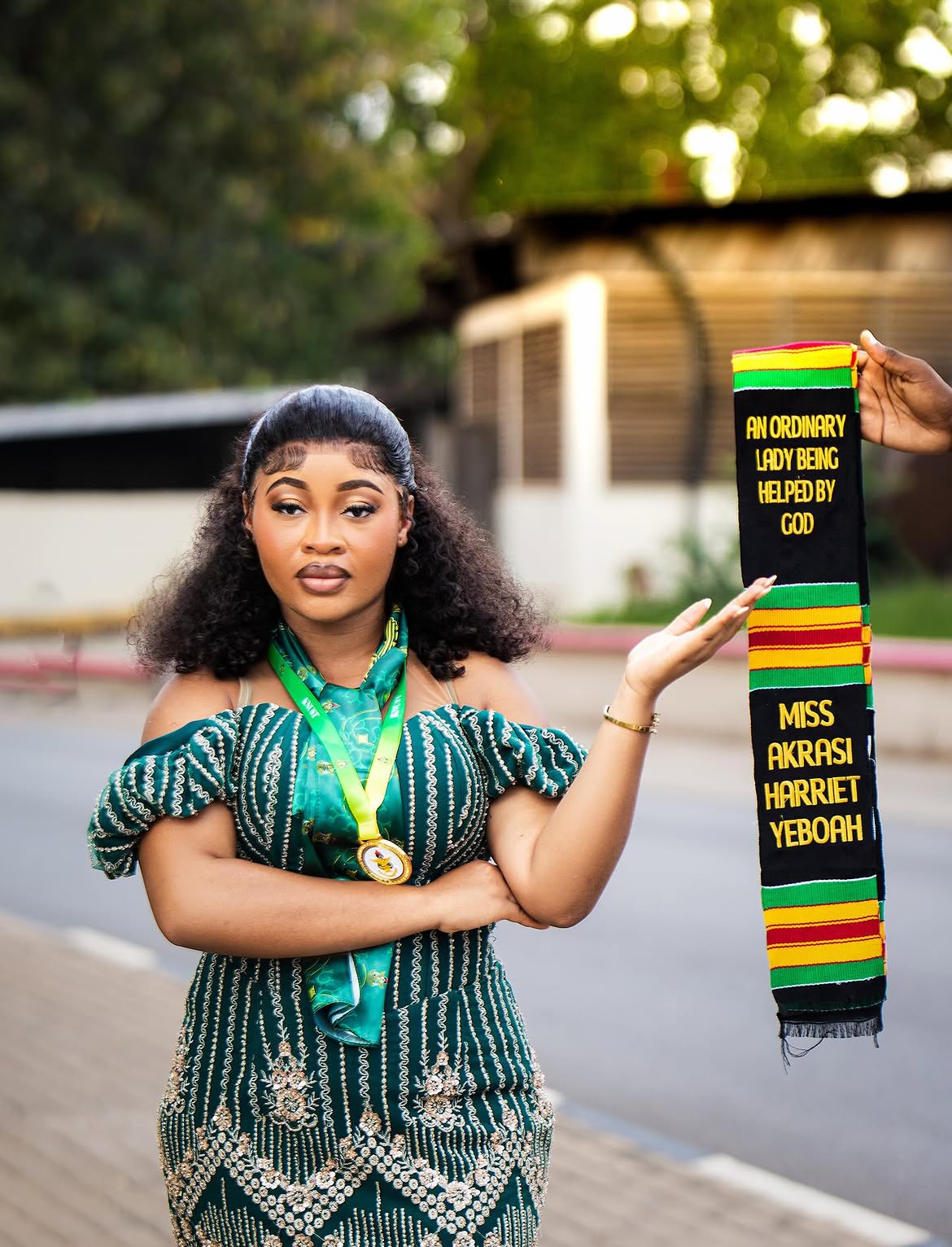 Graduate Miss Harriet holding her kente graduation sash, direct editorial gaze